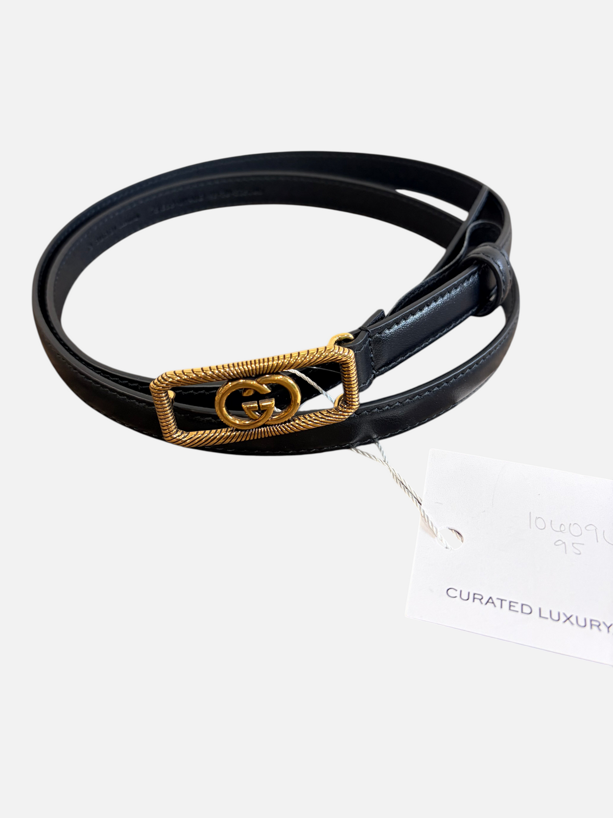 CURATED by Kira Gucci GG buckle leather belt in black with gold-tone textured hardware on a wooden surface.