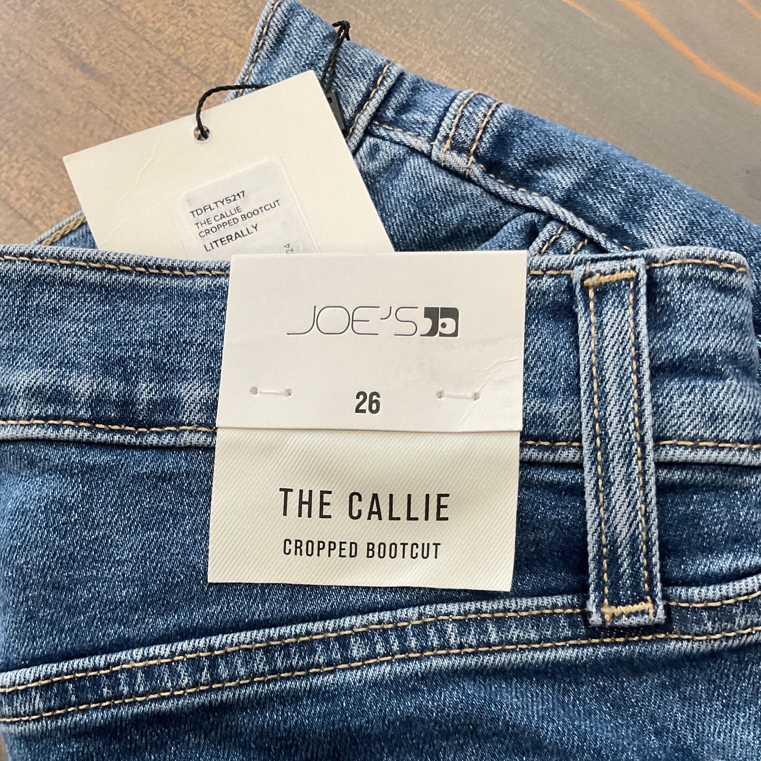 Close-up of blue jeans with a JOE'S tag on a neutral background