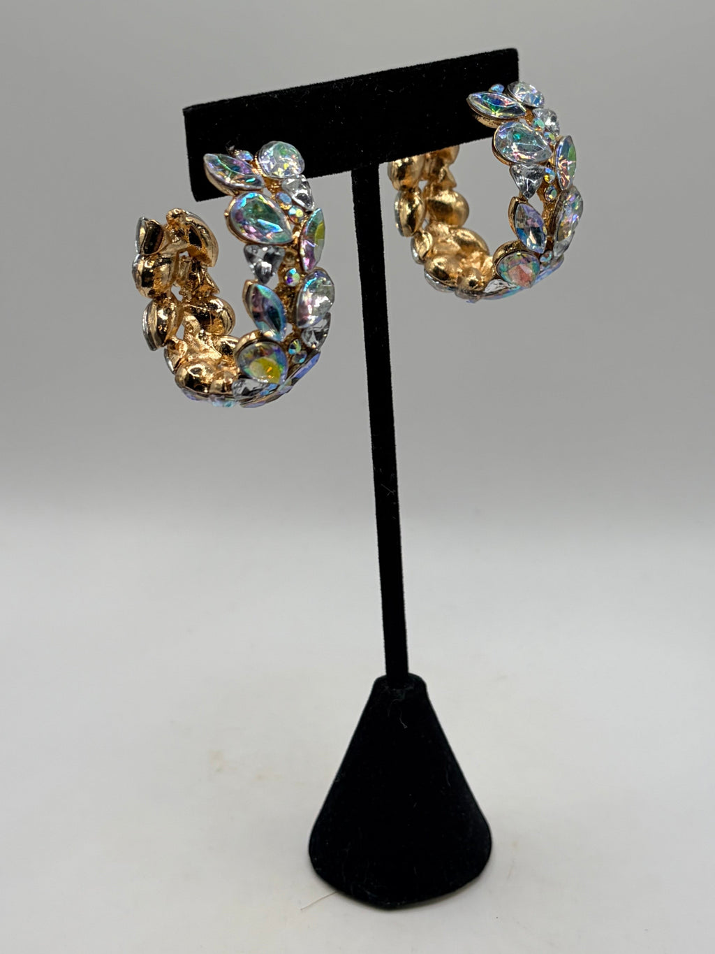 CURATED by Kira gold-plated hoop earrings featuring iridescent multi-colored stones on a black display stand.