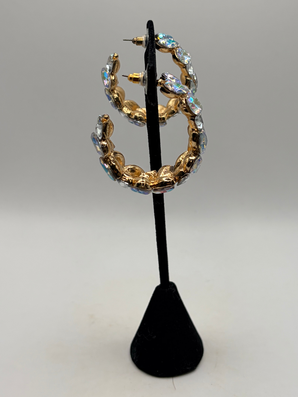 CURATED by Kira gold-plated hoop earrings featuring iridescent stones and push-back closures on a display stand.