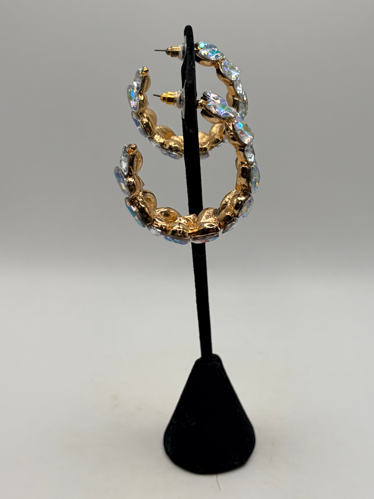 CURATED by Kira gold-plated hoop earrings featuring iridescent stones and push-back closures on a display stand.