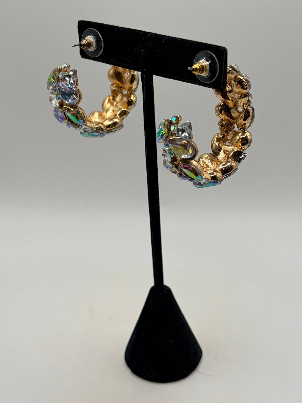 CURATED by Kira gold-plated hoop earrings featuring iridescent stones on a black display stand with push-back closure.