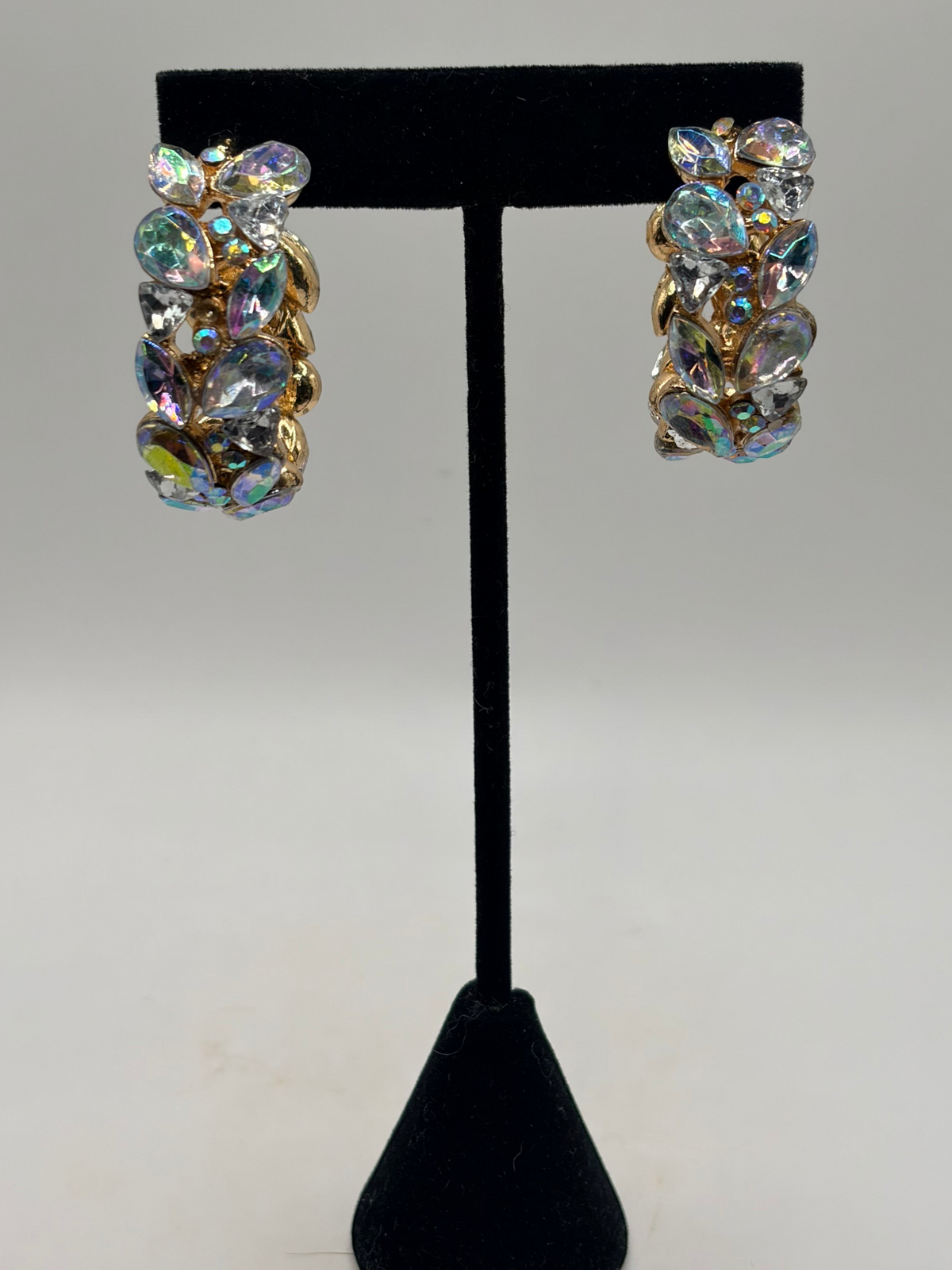 CURATED by Kira gold-plated hoop earrings featuring clusters of iridescent stones on a black display stand