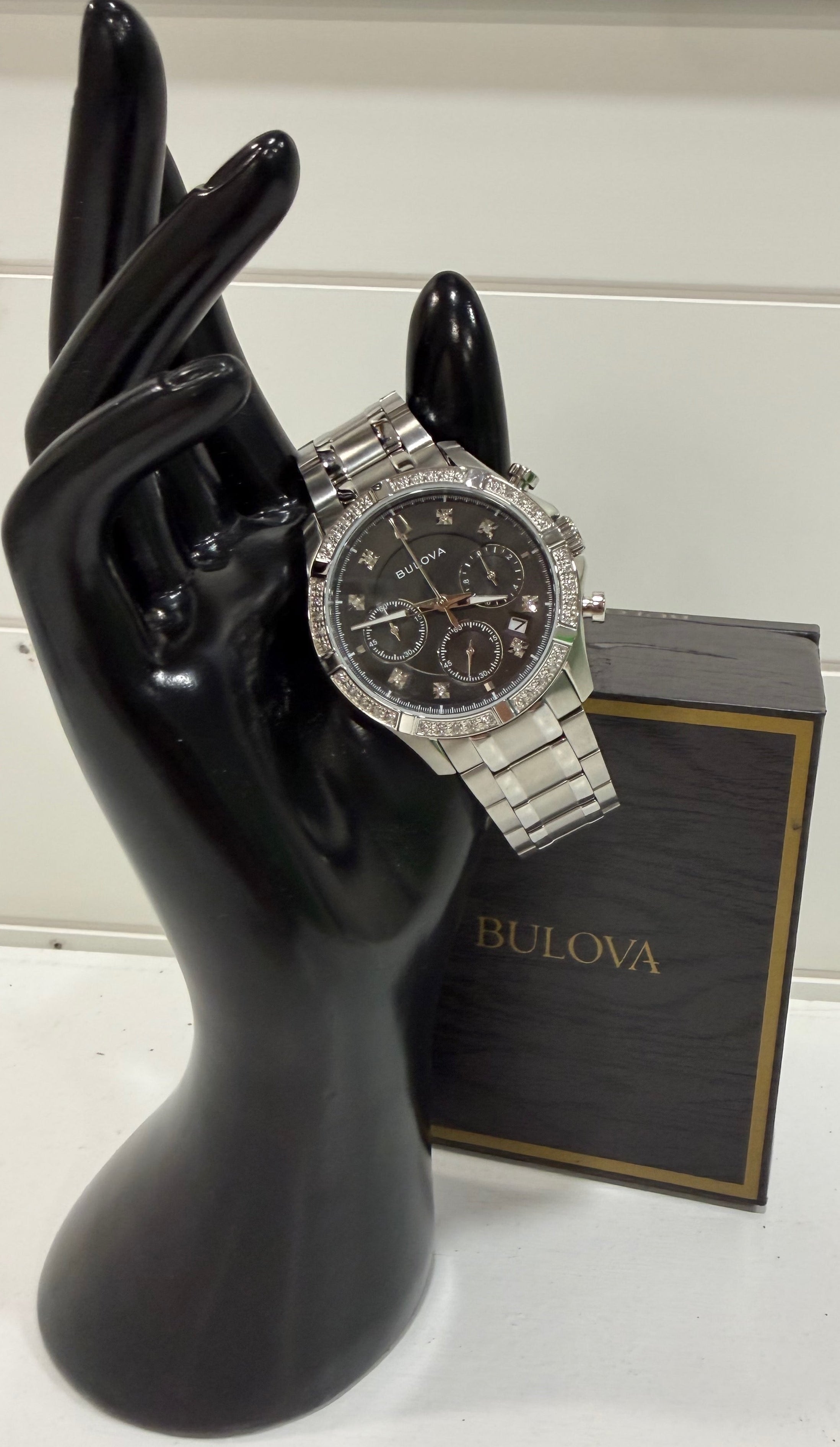 Silver Bulova watch on a black mannequin hand with a white background
