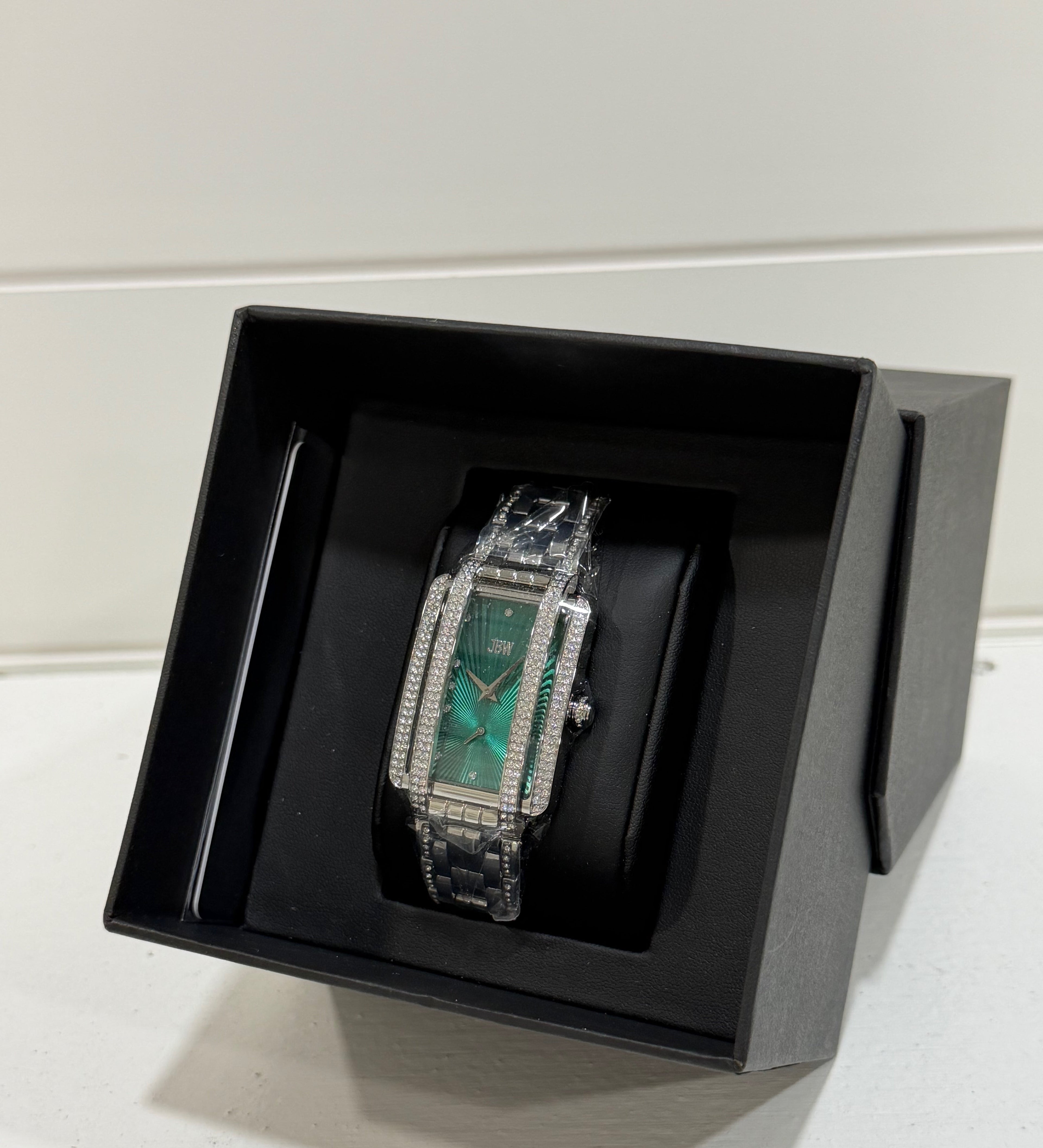 Luxury watch with green face and silver case in a black box on a white surface