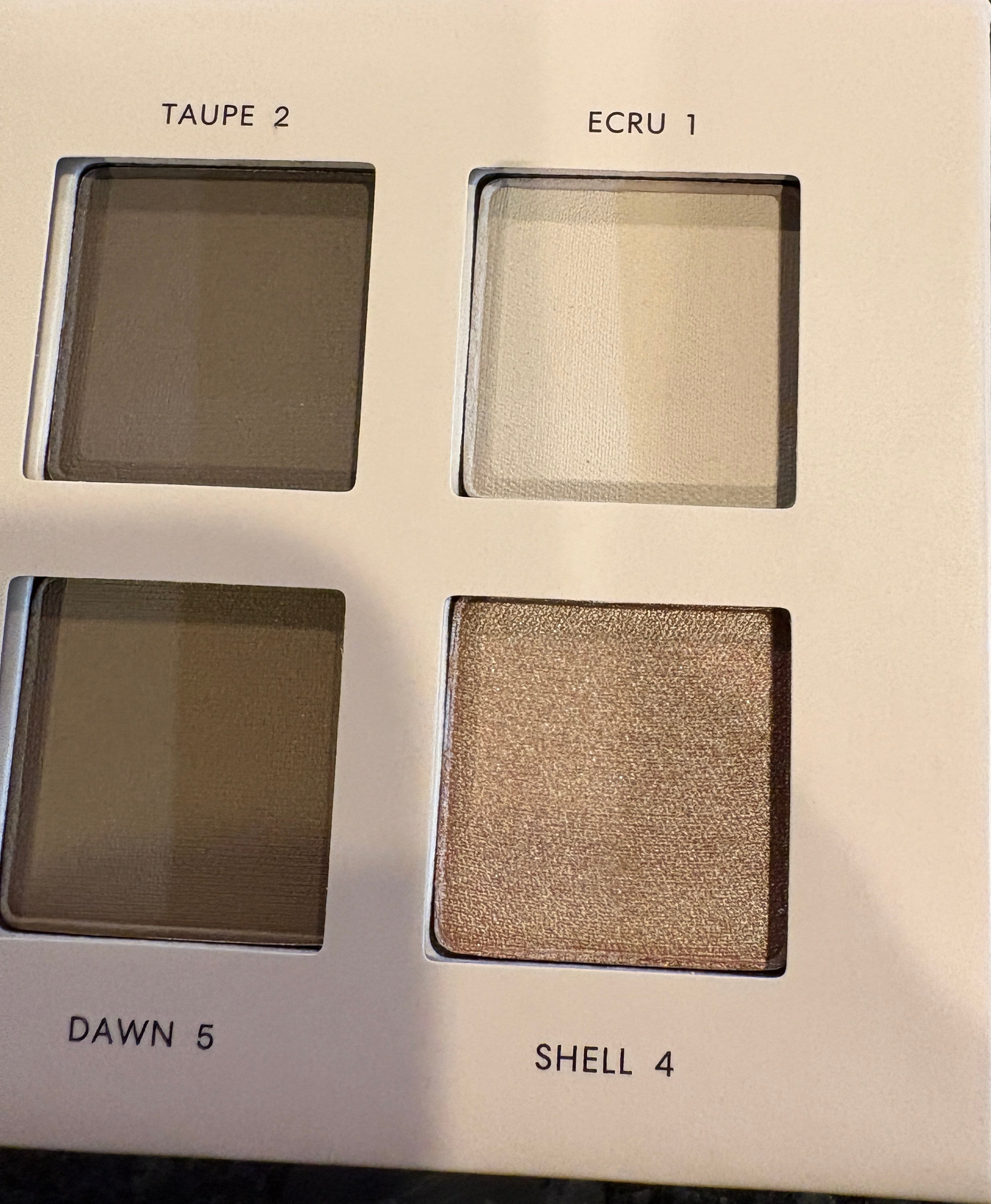 Makeup palette with four eyeshadow shades on a dark surface