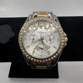 Fossil women's watch with a silver and rose gold-tone case, a crystal-studded bezel, and a white dial, displayed on a black stand.