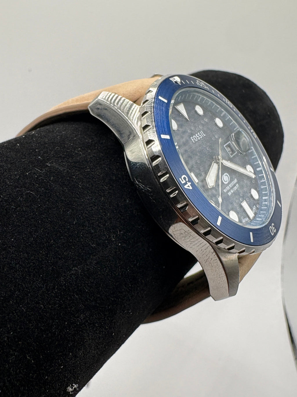CURATED by Kira Fossil Blue dive watch with a blue bezel, black dial, and tan leather strap on a display stand.