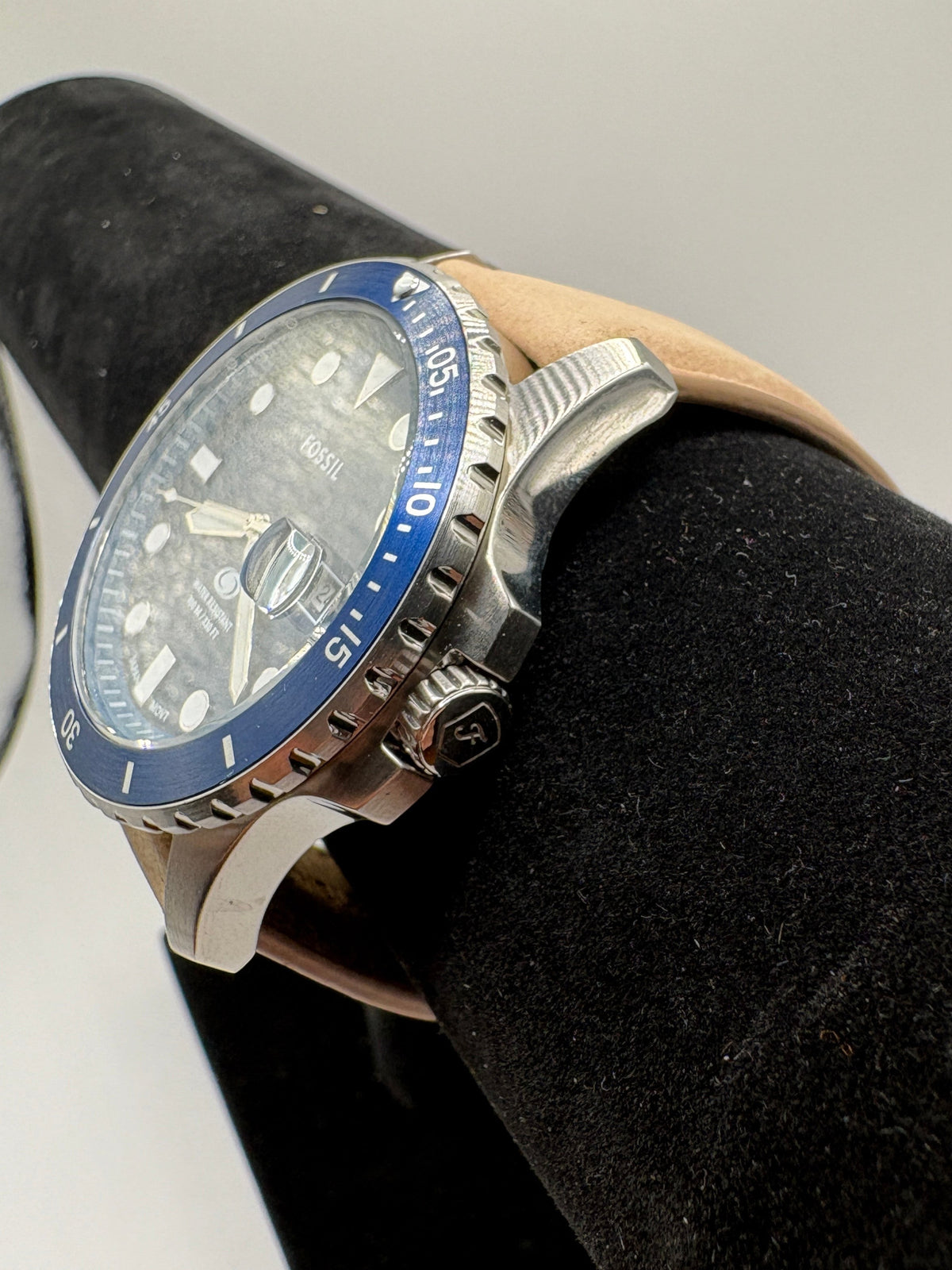 CURATED by Kira Fossil Blue dive watch with a textured grey dial, blue bezel, and a tan leather strap on a stand