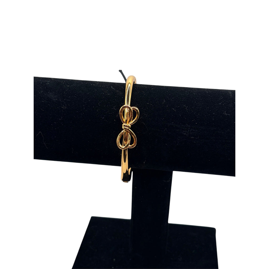 CURATED by Kira gold tone Kate Spade hinged bangle bracelet featuring a delicate bow knot design on a display stand.