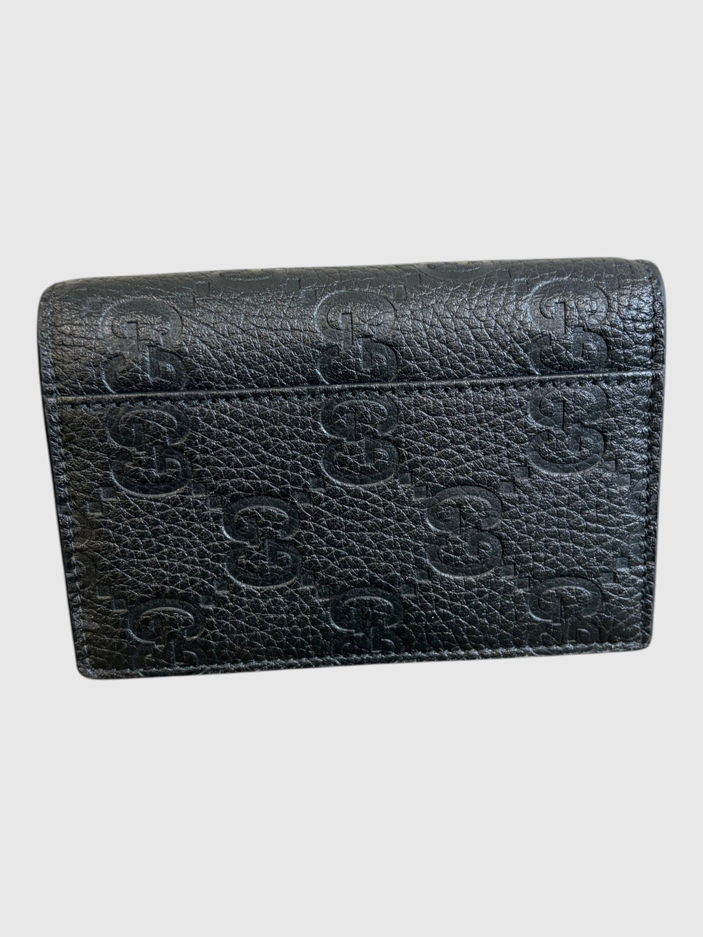 CURATED by Kira black grainy calfskin Gucci card case with embossed GG logo pattern on a wooden surface