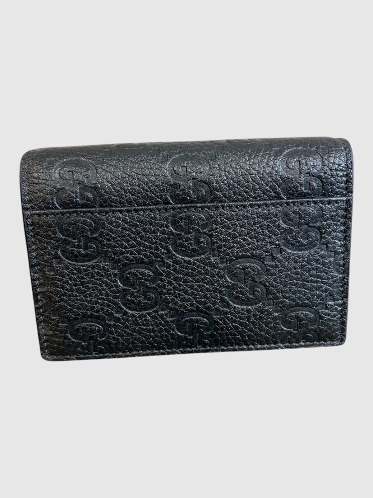 CURATED by Kira black grainy calfskin Gucci card case with embossed GG logo pattern on a wooden surface