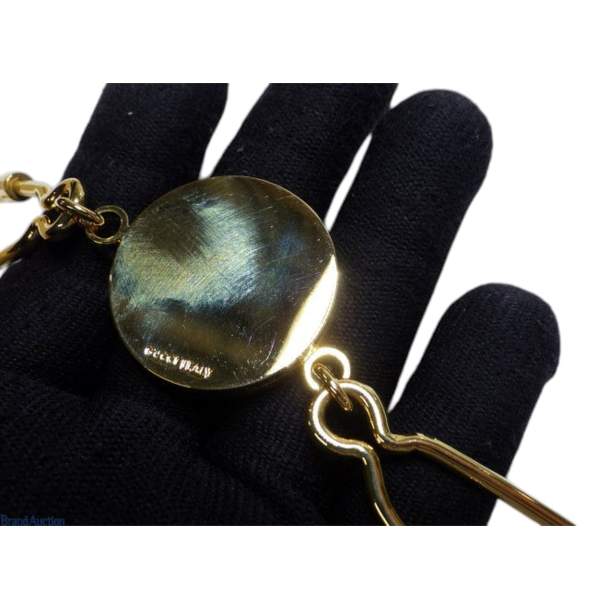 CURATED by Kira gold Gucci Interlocking G keyring held in a black gloved hand showing the engraved back detail