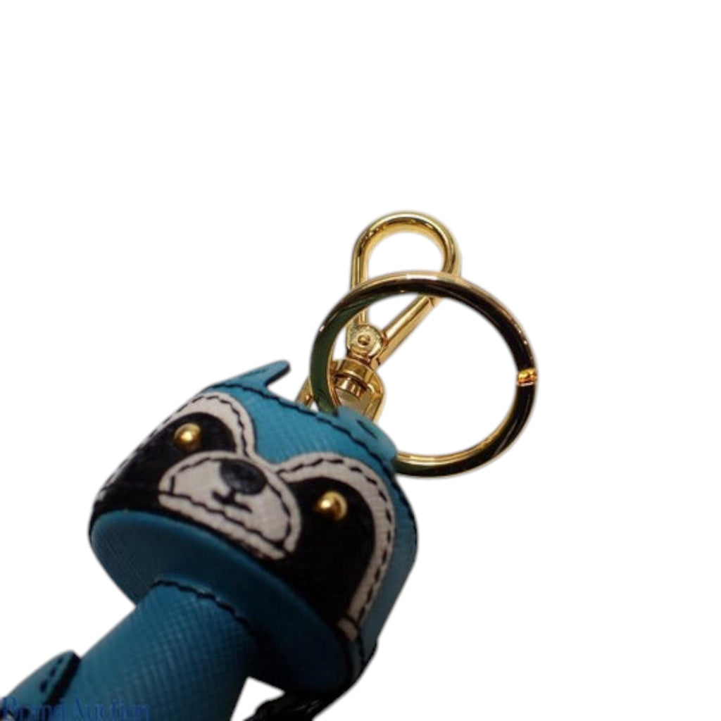 CURATED by Kira Prada raccoon key ring in teal Saffiano leather with gold-tone hardware and black and white details.