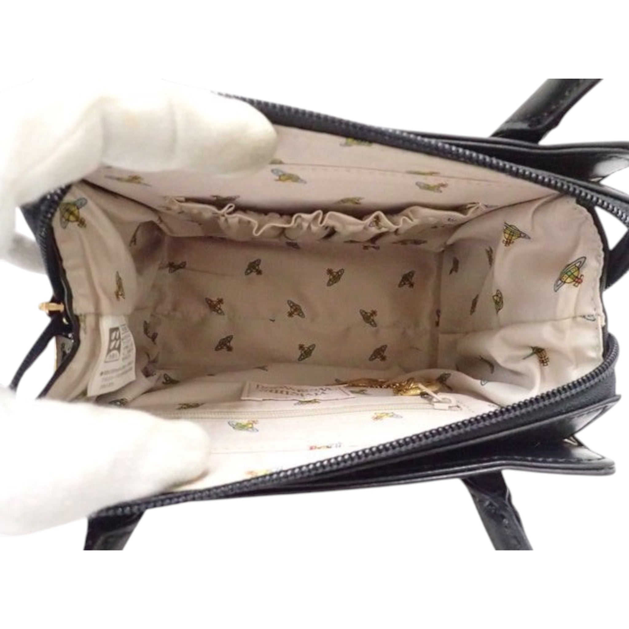 Interior of a black Vivienne Westwood enamel handbag featuring a beige logo-patterned lining, sold by CURATED by Kira.