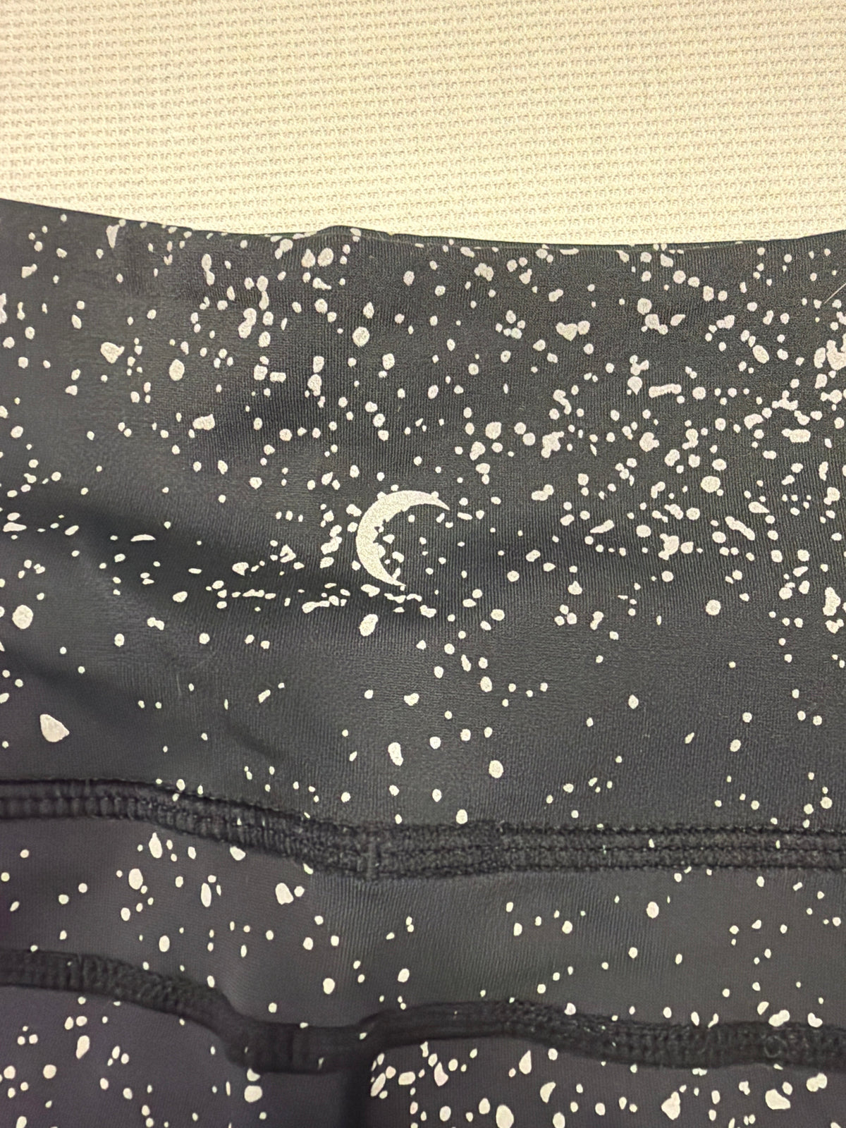 CURATED by Kira Zyia Active black high-rise leggings featuring a white reflective paint splatter pattern and crescent logo